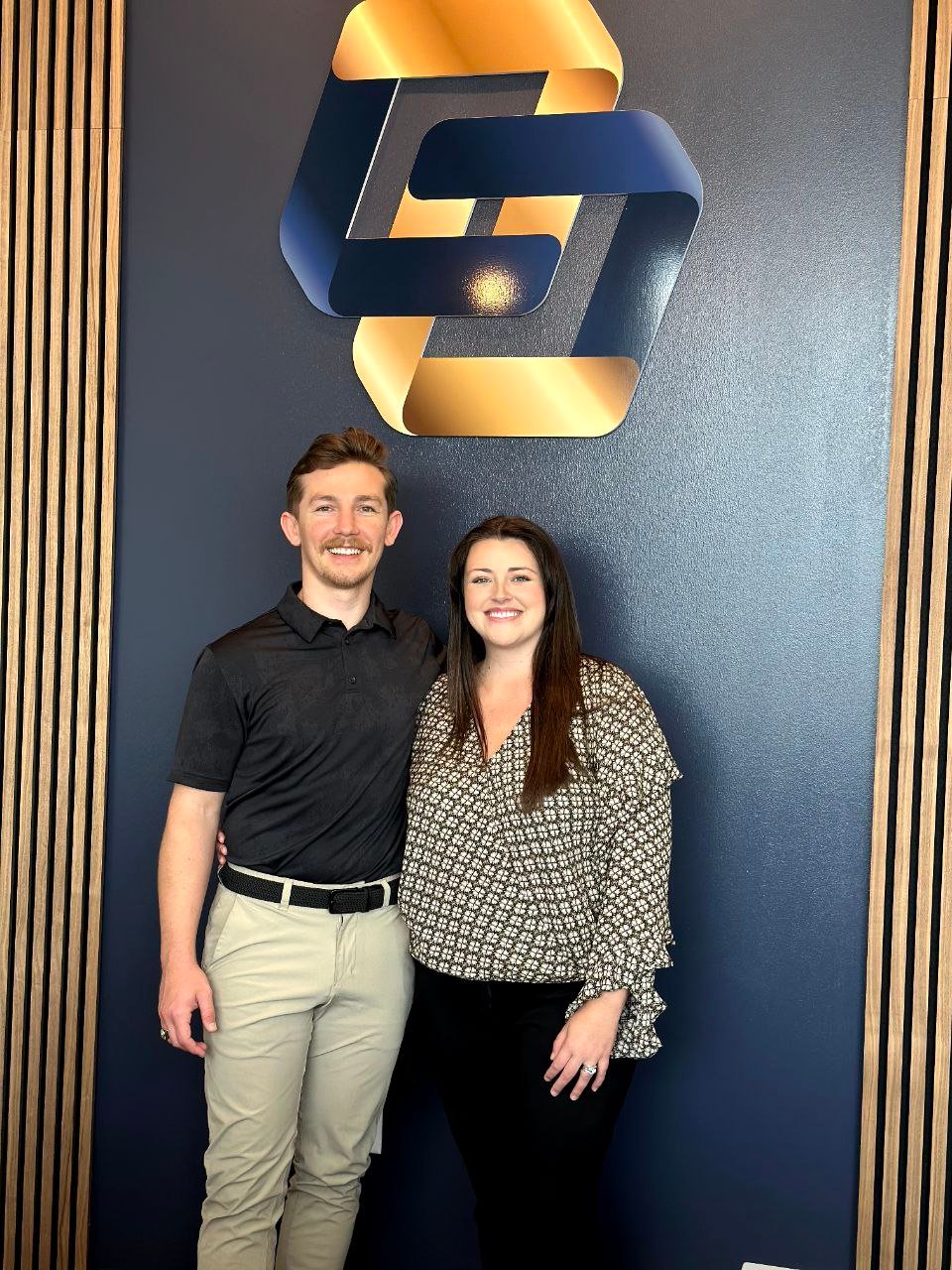 Two dedicated owners from Limitless Chiropractic, your trusted chiropractor in Alliance, standing proudly in their North Fort Worth clinic before the modern gold and blue interconnected C-shape logo.