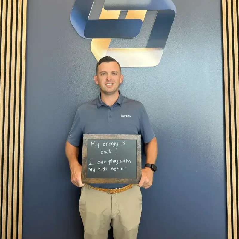 Male patient at Limitless Chiropractic, your chiropractor in North Fort Worth, holding a sign: "My energy is back! I can play with my kids again!" - also serving Alliance.
