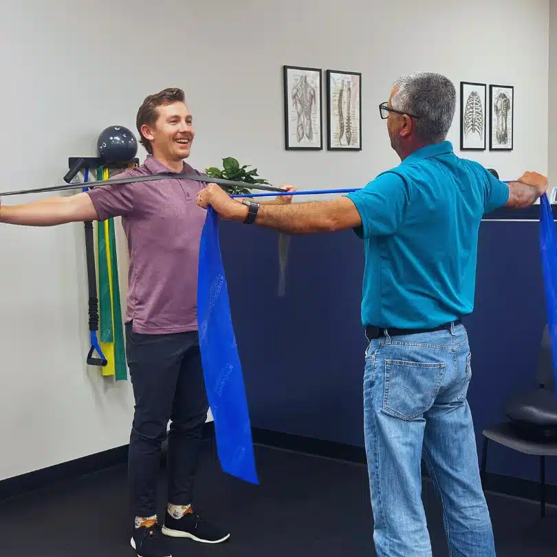 Chiropractor supervising shoulder resistance band exercise for rehab in Alliance Town Center